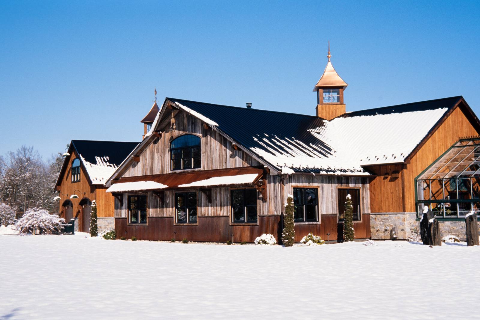 Party Barn in the Snow • Exterior Features Include: Reclaimed Barn Siding • Rusty Metal Accents • Timber Frame Eyebrow Roof & Accents
