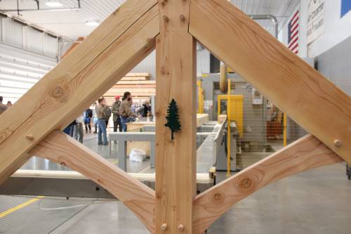 Timber truss on display with the company's green tree logo. CNC machine in the background.