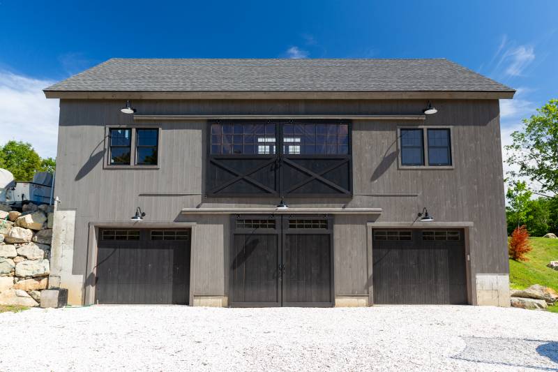 Back of the barn with garage doors at ground level and sliding half glass doors on the first floor