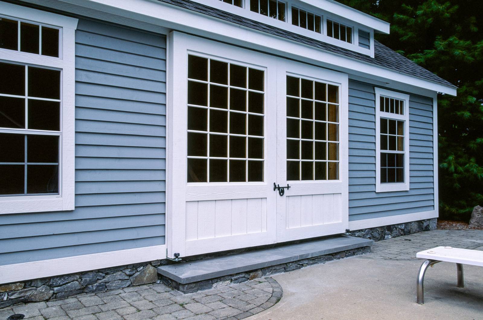 Notice the details: sliding barn doors with 20-lite glass • cedar clapboard siding with custom paint color • wide trim • rock facade on foundation