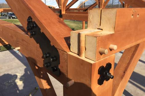 Closeup of traditional wood joinery and powder-coated steel reinforcements working together in the timber frame
