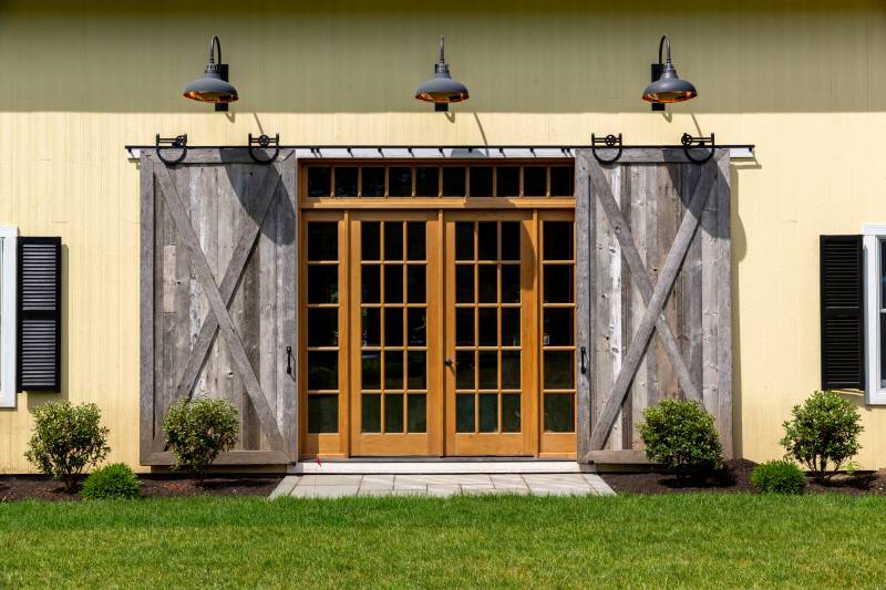 Sliding barn doors with authentic horseshoe track revealing full view glass double doors with sidelights & transoms