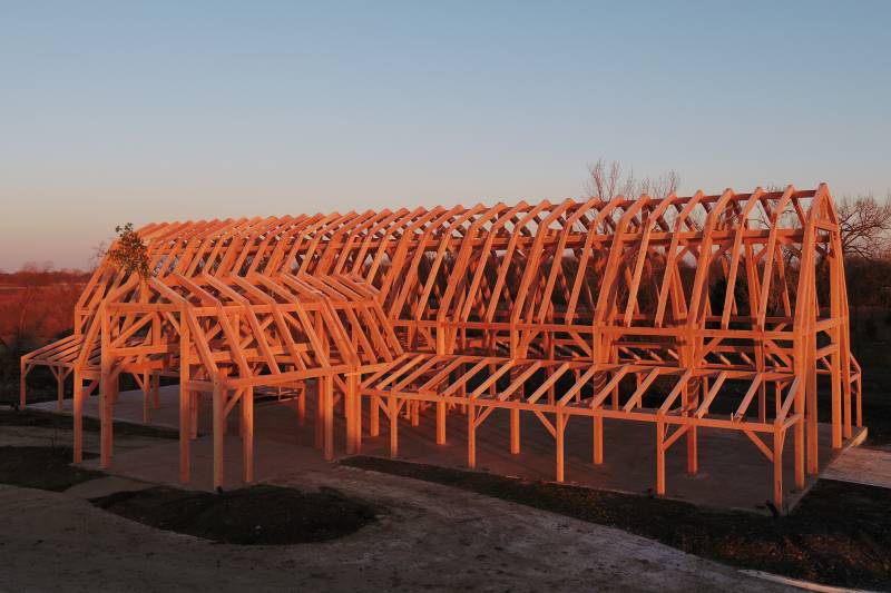 The rising sun illuminates the frame for this 64' x 152' timber frame event barn with 32' x 32' bump out