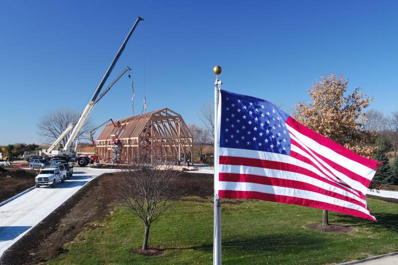 The American flag waves in the breeze as the crew works on setting rafters with double cranes